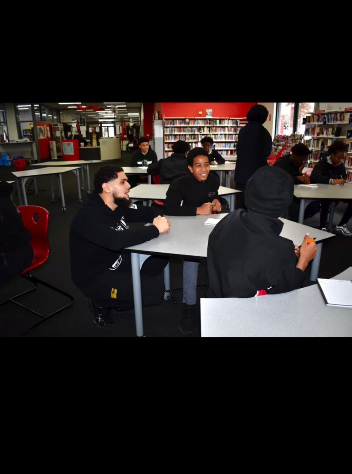 Three smiling students seated with Zayd at a library table