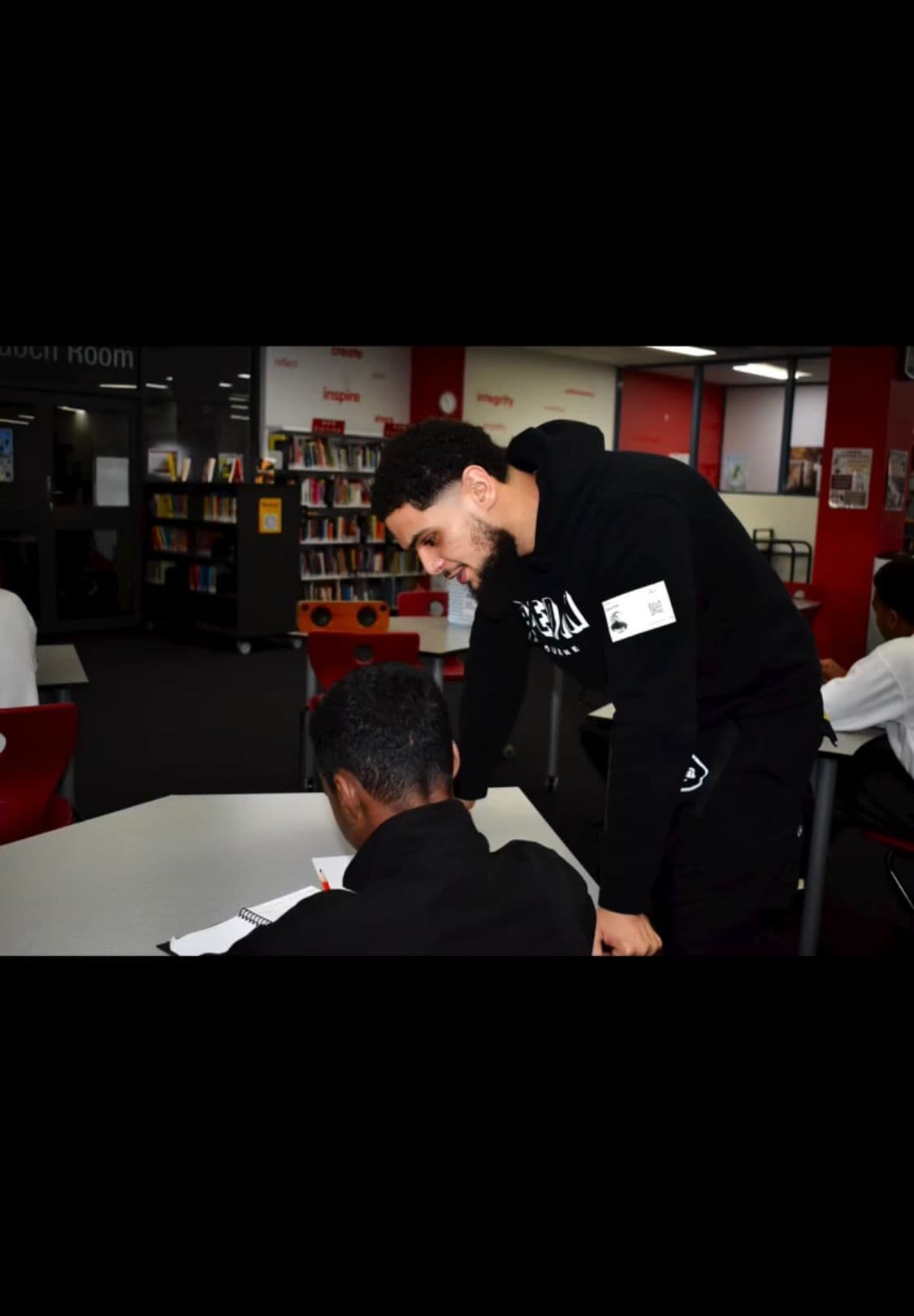 Zayd helping a seated student with written work
